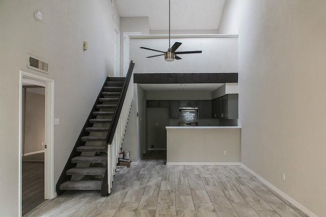 interior space featuring light wood-type flooring, ceiling fan, and a towering ceiling