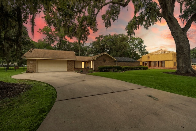 single story home with a garage, solar panels, and a lawn