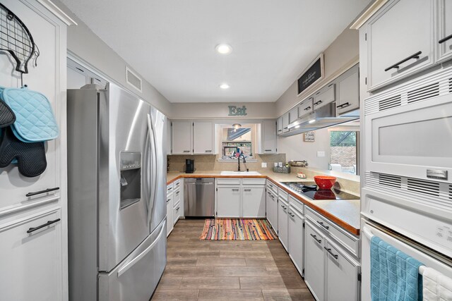 kitchen with white cabinets, dark hardwood / wood-style flooring, stainless steel appliances, decorative backsplash, and sink