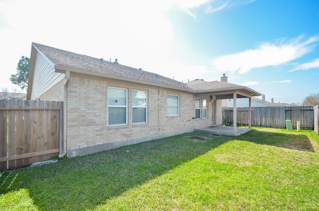 rear view of house featuring brick siding, a yard, a chimney, a patio, and a fenced backyard