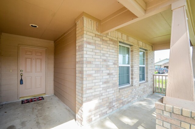 view of exterior entry featuring brick siding and a porch