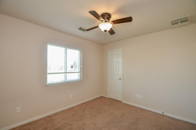 spare room featuring a ceiling fan, light colored carpet, visible vents, and baseboards