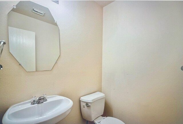 half bath with visible vents, a sink, and toilet