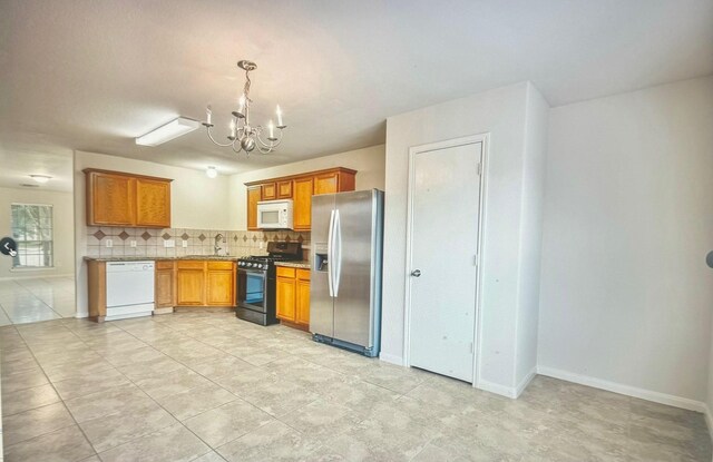 kitchen featuring decorative light fixtures, backsplash, an inviting chandelier, a sink, and white appliances