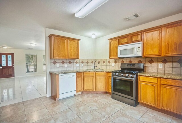 kitchen featuring white appliances, visible vents, decorative backsplash, brown cabinets, and a sink