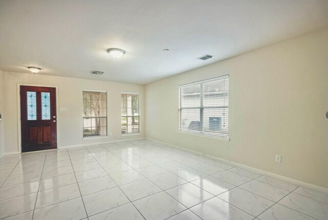 empty room featuring a wealth of natural light, visible vents, and baseboards