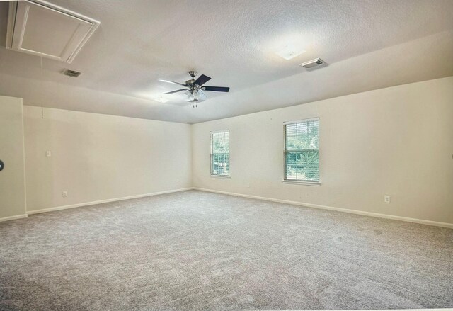 unfurnished room with visible vents, attic access, carpet flooring, ceiling fan, and a textured ceiling