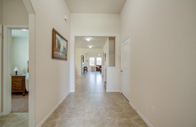 corridor with baseboards, arched walkways, and light tile patterned floors