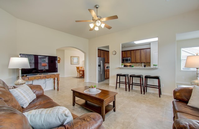 living area featuring arched walkways, ceiling fan, and light tile patterned floors