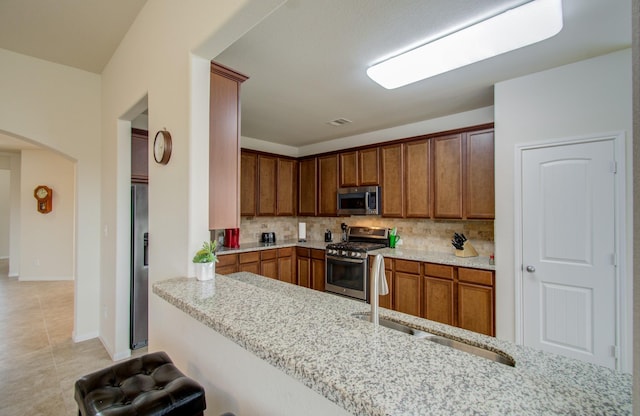 kitchen with light stone countertops, tasteful backsplash, arched walkways, light tile patterned floors, and stainless steel appliances