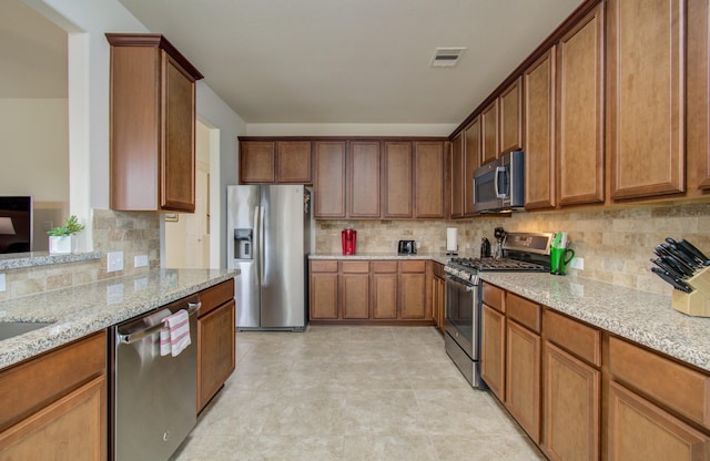 kitchen featuring light stone counters, backsplash, visible vents, and stainless steel appliances