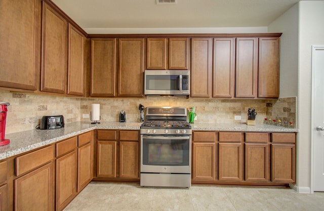 kitchen featuring appliances with stainless steel finishes, brown cabinetry, light stone counters, and tasteful backsplash