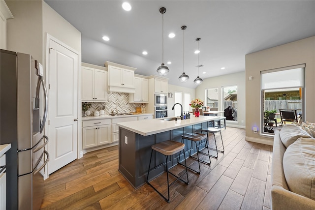 kitchen with pendant lighting, backsplash, a center island with sink, a breakfast bar, and appliances with stainless steel finishes