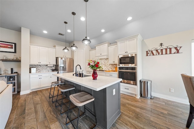 kitchen with stainless steel appliances, white cabinetry, pendant lighting, an island with sink, and a breakfast bar