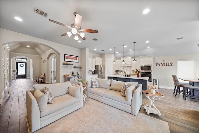 living room with lofted ceiling, sink, ceiling fan, and light wood-type flooring