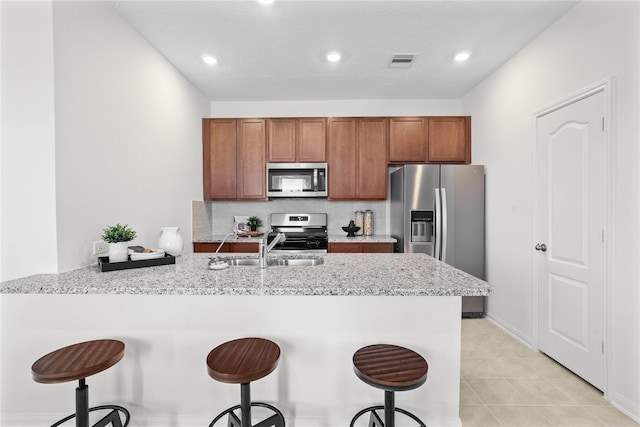 kitchen with sink, a kitchen breakfast bar, light stone counters, kitchen peninsula, and appliances with stainless steel finishes