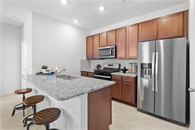 kitchen featuring sink, light stone counters, a textured ceiling, a kitchen bar, and appliances with stainless steel finishes