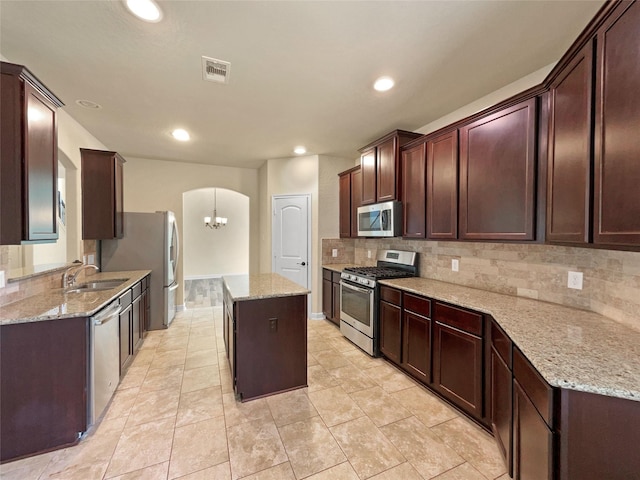 kitchen featuring sink, stainless steel appliances, a center island, and light stone counters