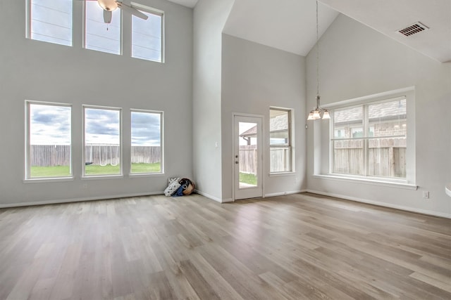 unfurnished living room featuring high vaulted ceiling, ceiling fan with notable chandelier, and light wood-type flooring