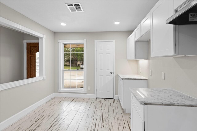 kitchen with white cabinetry, extractor fan, light stone counters, and light wood-type flooring