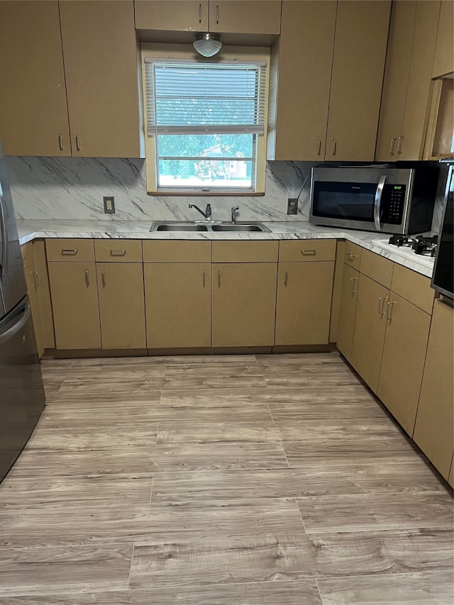 kitchen featuring appliances with stainless steel finishes, light hardwood / wood-style flooring, decorative backsplash, and sink