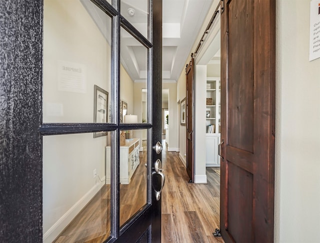 exercise area with a barn door, wood-type flooring, and ornamental molding