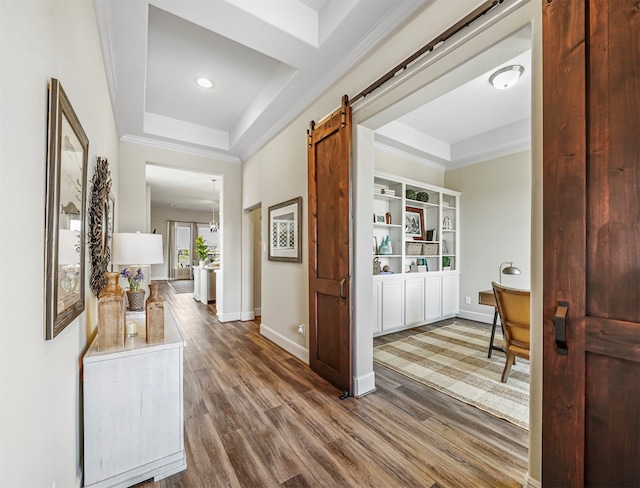 hall featuring a raised ceiling, a barn door, crown molding, and wood-type flooring