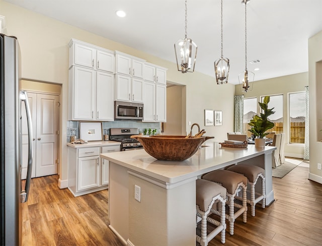 kitchen with hanging light fixtures, an island with sink, appliances with stainless steel finishes, light hardwood / wood-style floors, and white cabinetry