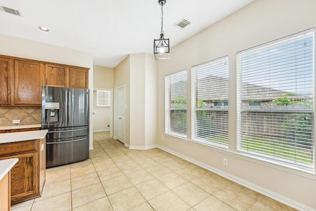 kitchen with a wealth of natural light, light tile patterned floors, pendant lighting, and stainless steel refrigerator with ice dispenser