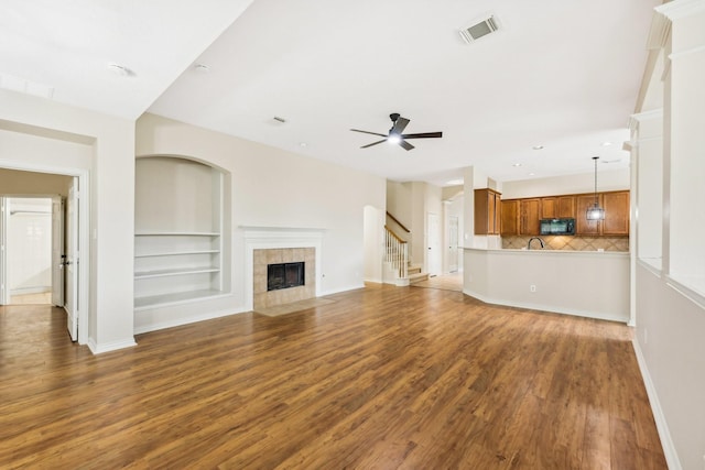 unfurnished living room featuring sink, ceiling fan, dark hardwood / wood-style floors, built in features, and a fireplace