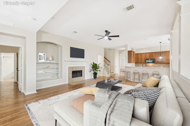 living room featuring ceiling fan, light hardwood / wood-style floors, built in features, and a tile fireplace