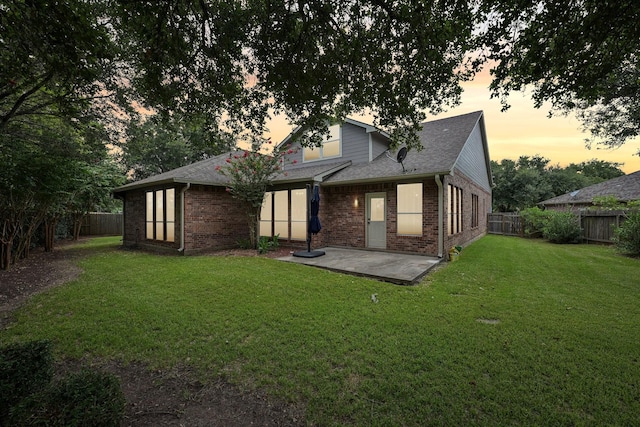 back house at dusk with a lawn and a patio