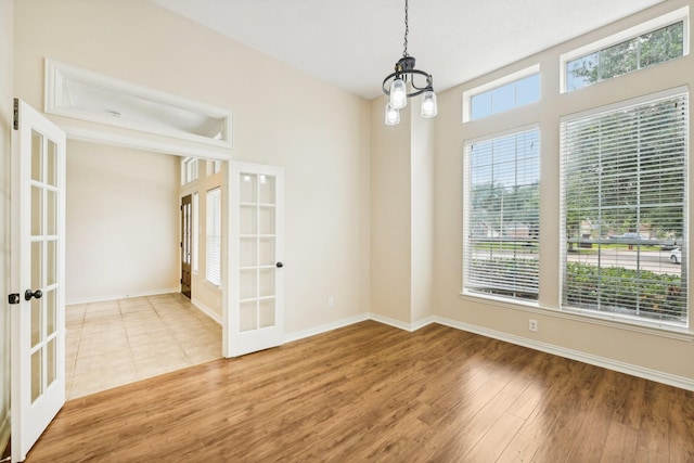 empty room with french doors, a notable chandelier, and wood-type flooring