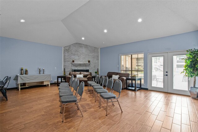 living room featuring light wood-type flooring, a brick fireplace, french doors, vaulted ceiling, and brick wall