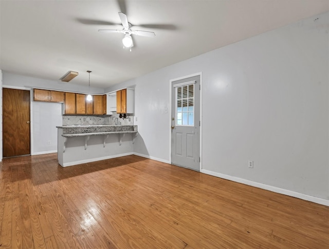 kitchen with a breakfast bar, ceiling fan, light hardwood / wood-style floors, decorative light fixtures, and kitchen peninsula