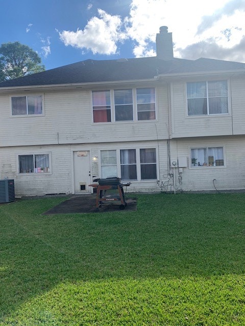 rear view of property featuring central air condition unit and a lawn