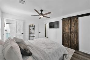 bedroom with ceiling fan, a barn door, and dark hardwood / wood-style flooring