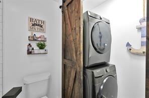 washroom with a barn door and stacked washer / drying machine