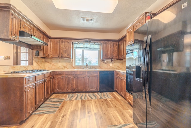 kitchen with tasteful backsplash, light wood-type flooring, a textured ceiling, black appliances, and sink