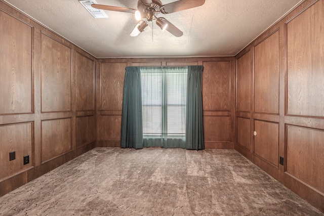 carpeted spare room featuring a textured ceiling, wooden walls, and ceiling fan