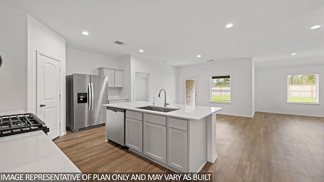 kitchen with sink, light hardwood / wood-style floors, gray cabinets, a kitchen island with sink, and appliances with stainless steel finishes