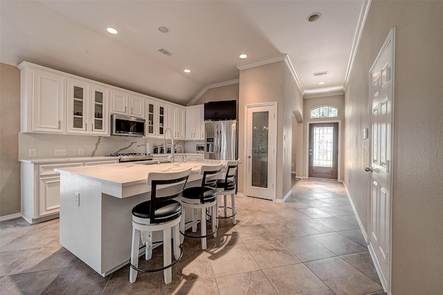 kitchen with white cabinetry, stainless steel appliances, ornamental molding, an island with sink, and a kitchen bar