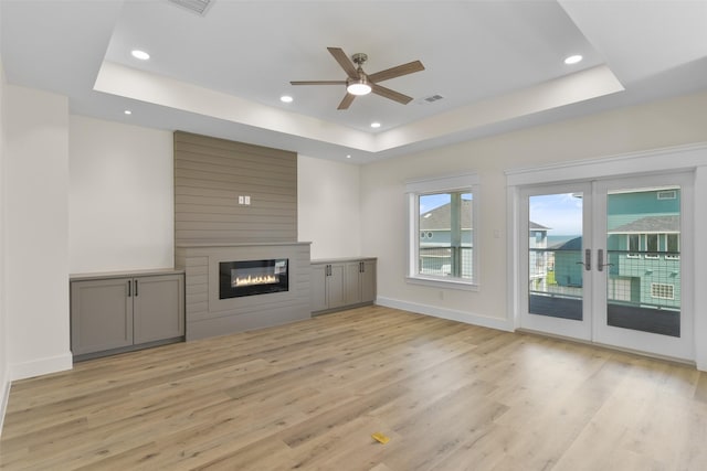 unfurnished living room with a fireplace, light wood-type flooring, and a tray ceiling