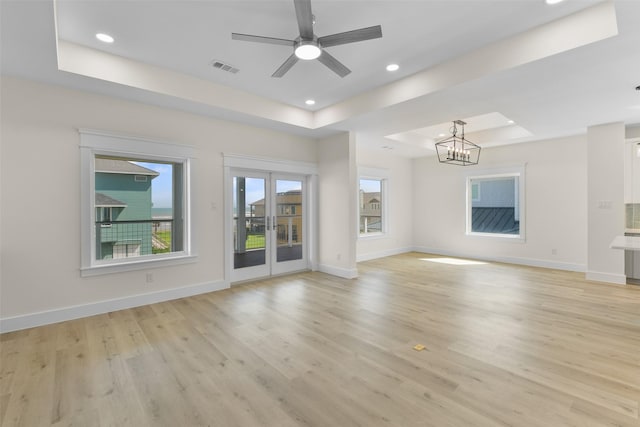 unfurnished living room with light wood-type flooring, a raised ceiling, and ceiling fan with notable chandelier