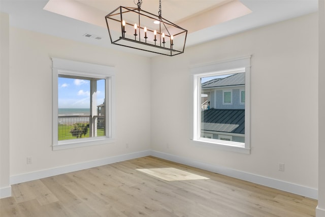 spare room featuring light wood-type flooring, a raised ceiling, a chandelier, and a water view