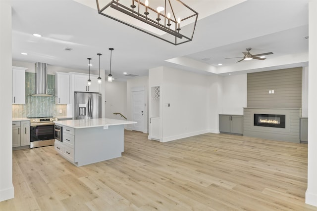 kitchen with a fireplace, a center island, wall chimney range hood, pendant lighting, and appliances with stainless steel finishes