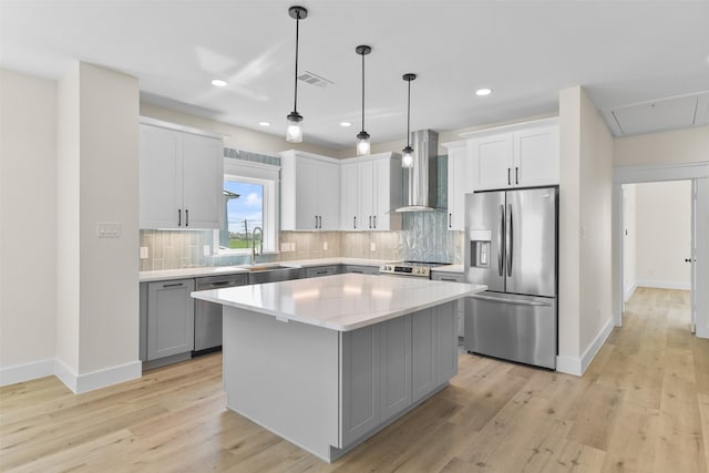 kitchen with appliances with stainless steel finishes, hanging light fixtures, light hardwood / wood-style floors, a kitchen island, and wall chimney exhaust hood