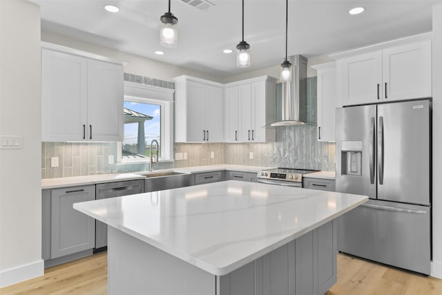 kitchen featuring appliances with stainless steel finishes, wall chimney exhaust hood, a kitchen island, sink, and decorative light fixtures