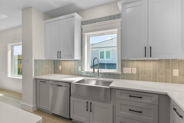 kitchen featuring dishwasher, light wood-type flooring, light stone countertops, sink, and backsplash