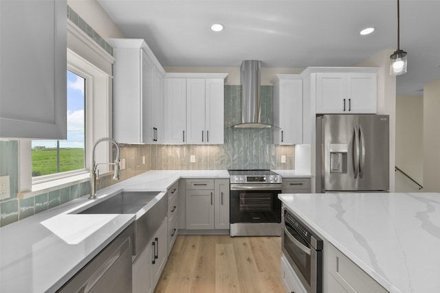 kitchen featuring appliances with stainless steel finishes, sink, white cabinetry, wall chimney range hood, and decorative light fixtures